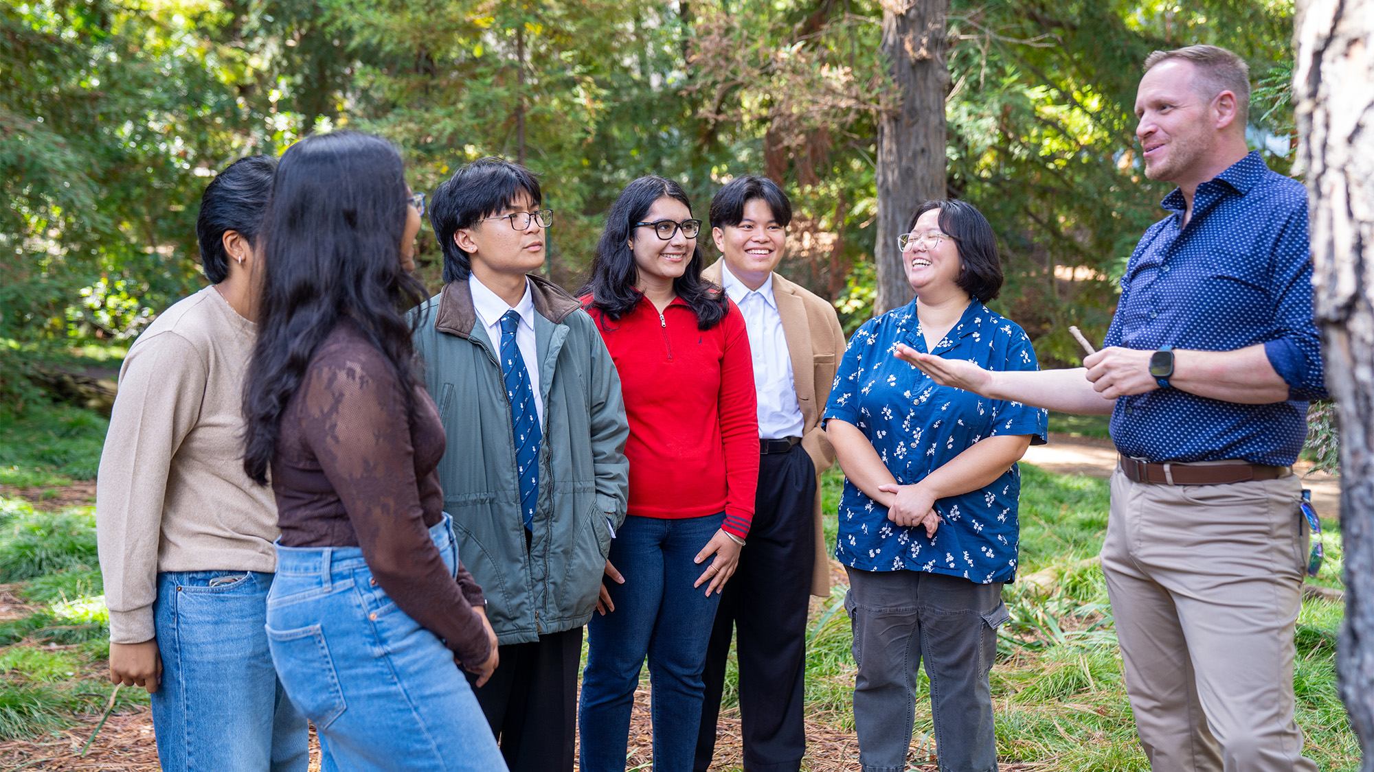 Diverse adults outdoors listening to a man speaking, candid photo