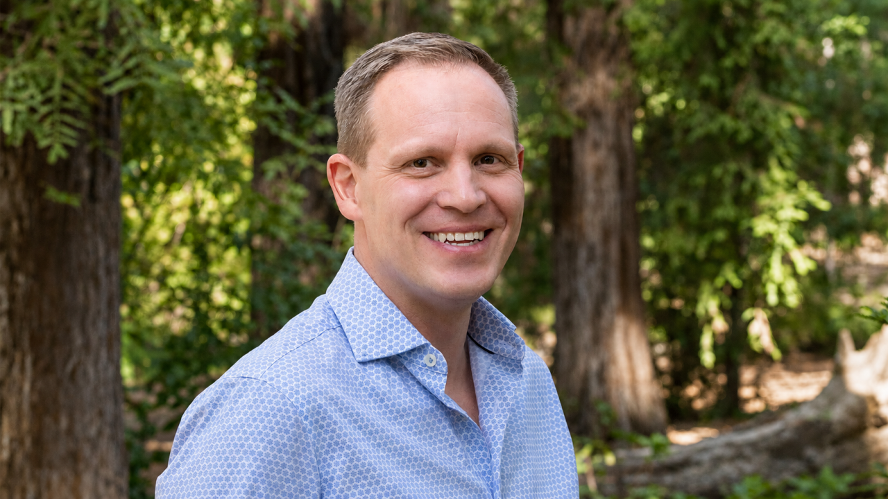 Smiling man in blue shirt outdoors among tall trees